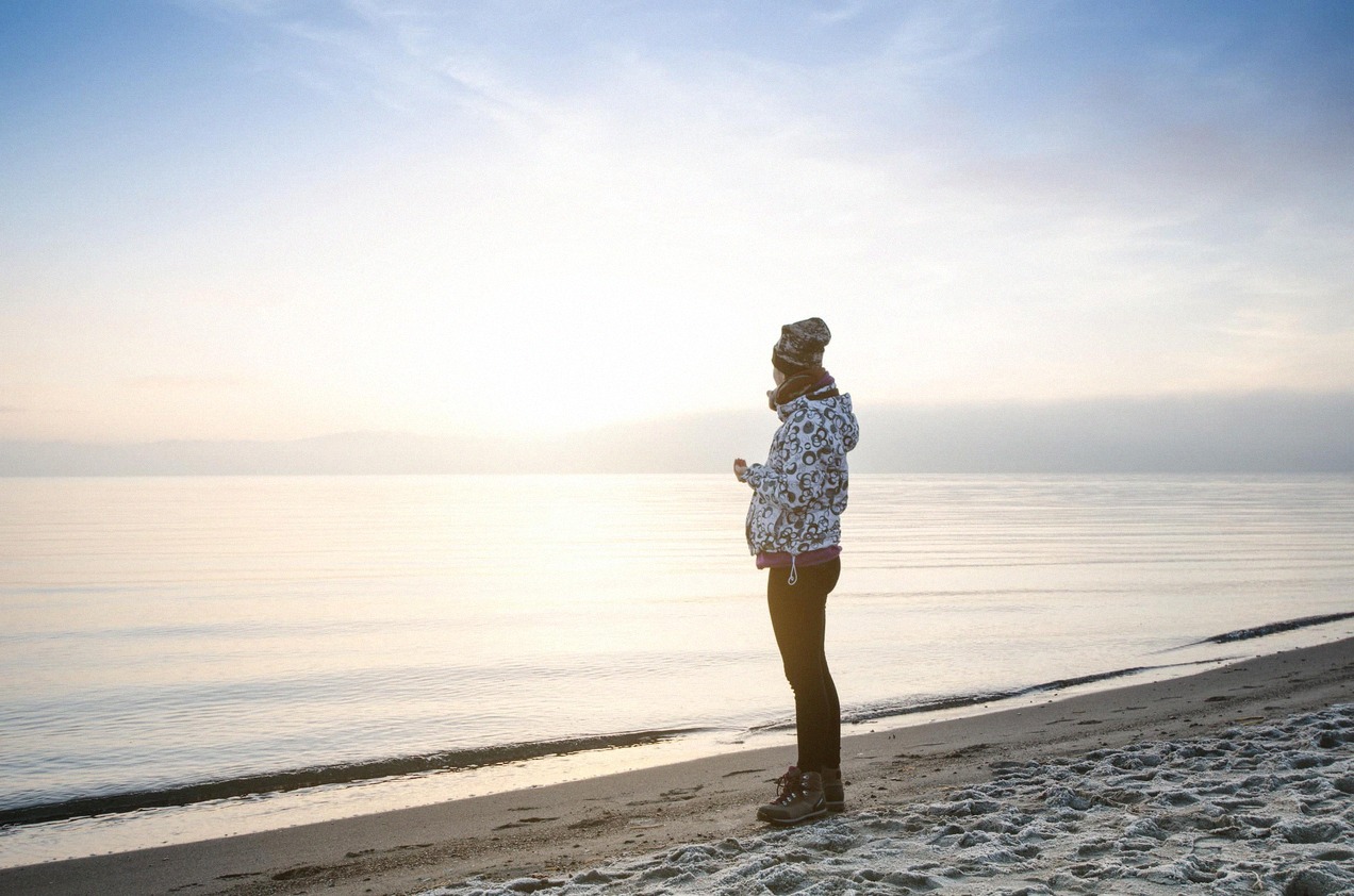 Spaziergängerin an einem dänischen Strand bei Sonnenaufgang im Winter