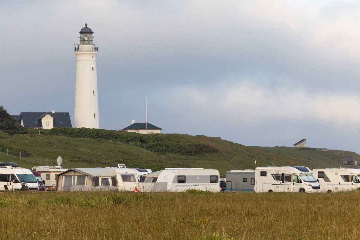 Wohnmobile und Wohnwagen auf einer Wiese unterhalb des weißen Leuchtturms von Hirtshals
